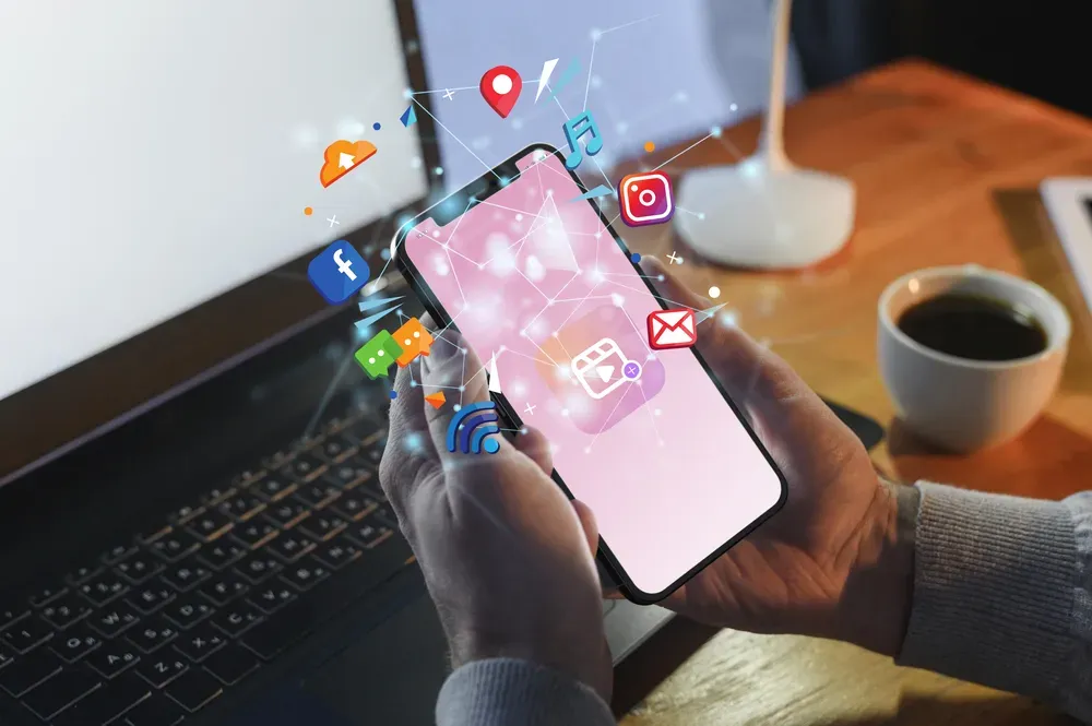 A person at a desk holding a phone and surrounded by 3D graphics from various phone applications.